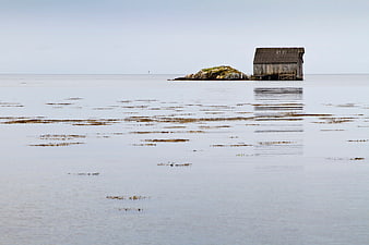 Lonely wooden shed on rocky island in calm sea
