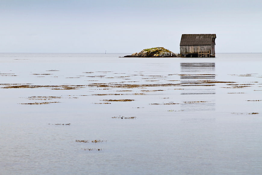 Lonely wooden shed on rocky island in calm sea