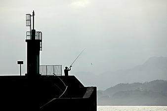 Silhouette of Man Fishing on Pier with Lighthouse