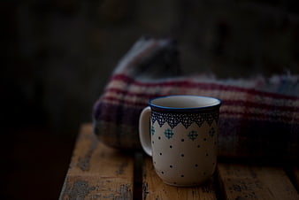 Rustic ceramic mug on wooden bench with plaid blanket