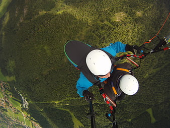 Tandem paragliding selfie over green forest mountains