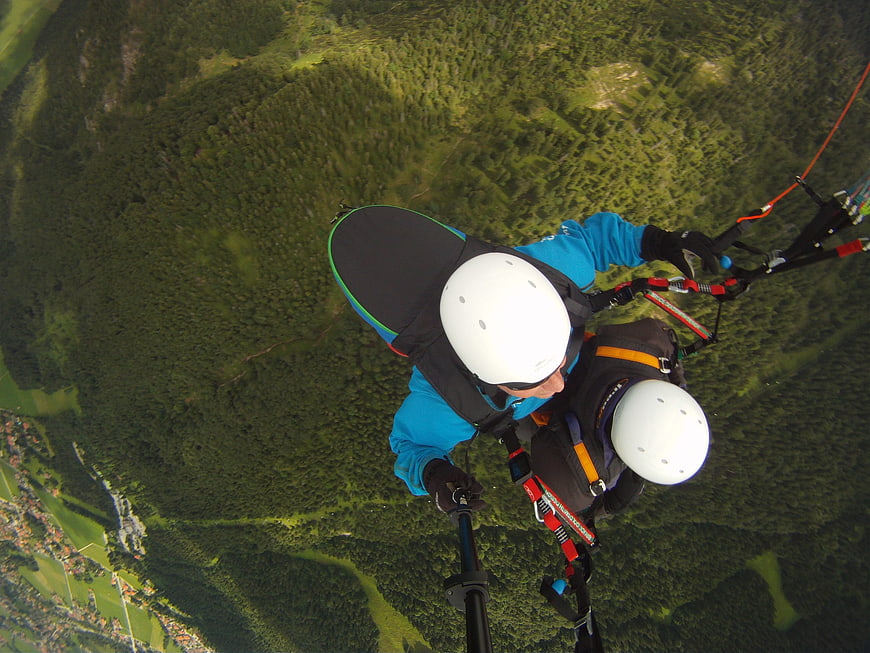 Tandem paragliding selfie over green forest mountains
