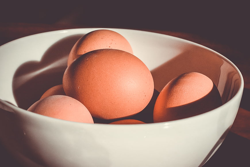 Brown eggs in a white ceramic bowl with dramatic lighting