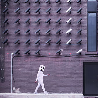 Person in Marshmello Mask Walking Past Wall of CCTV Cameras