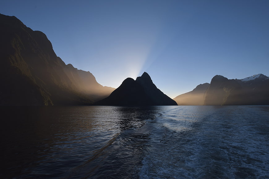 Dramatic Mountain Silhouette with Sun Rays Over Ocean Wake