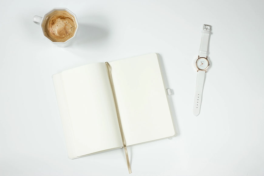 Minimalist flat lay with open notebook, coffee, and white watch