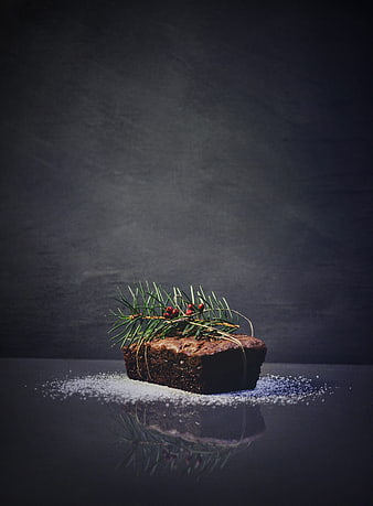 Dark chocolate brownie with pine sprig and red berries on reflective surface