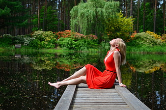 Woman in red dress relaxing on wooden dock by forest lake