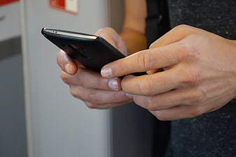 Close-up of hands using a black smartphone indoors