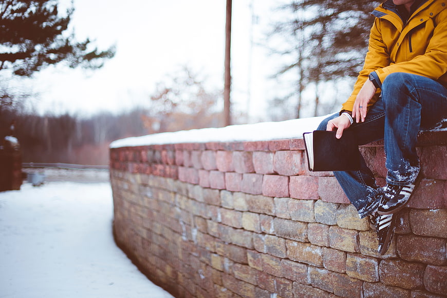 Man in Yellow Jacket Sitting on Stone Wall in Snow