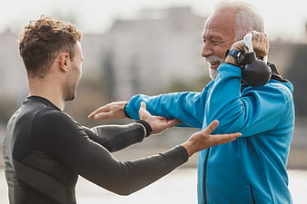 Senior man training with kettlebell and personal trainer outdoors