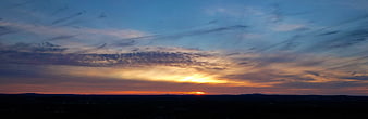 Panoramic sunset over dark landscape with dramatic clouds