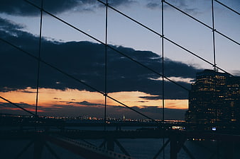 City skyline at dusk through bridge cables with sunset clouds