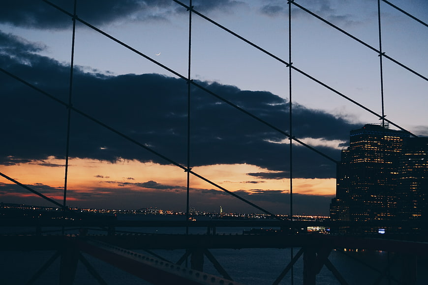 City skyline at dusk through bridge cables with sunset clouds