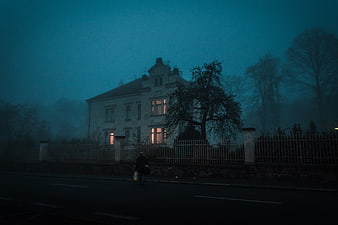 Lonely figure walking past old house in foggy blue twilight