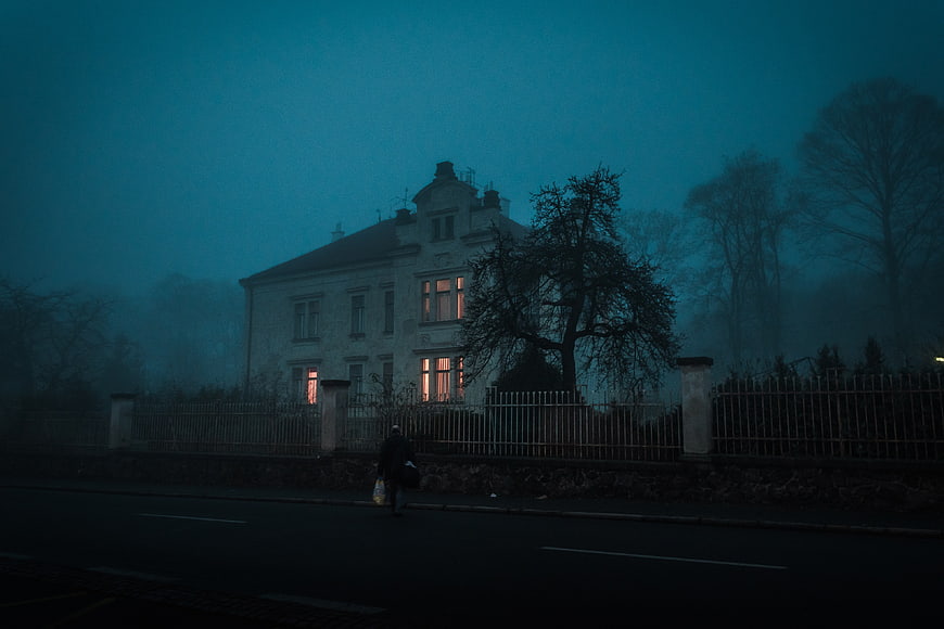 Lonely figure walking past old house in foggy blue twilight