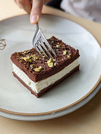 Close-up of chocolate cake with cream and pistachios being eaten