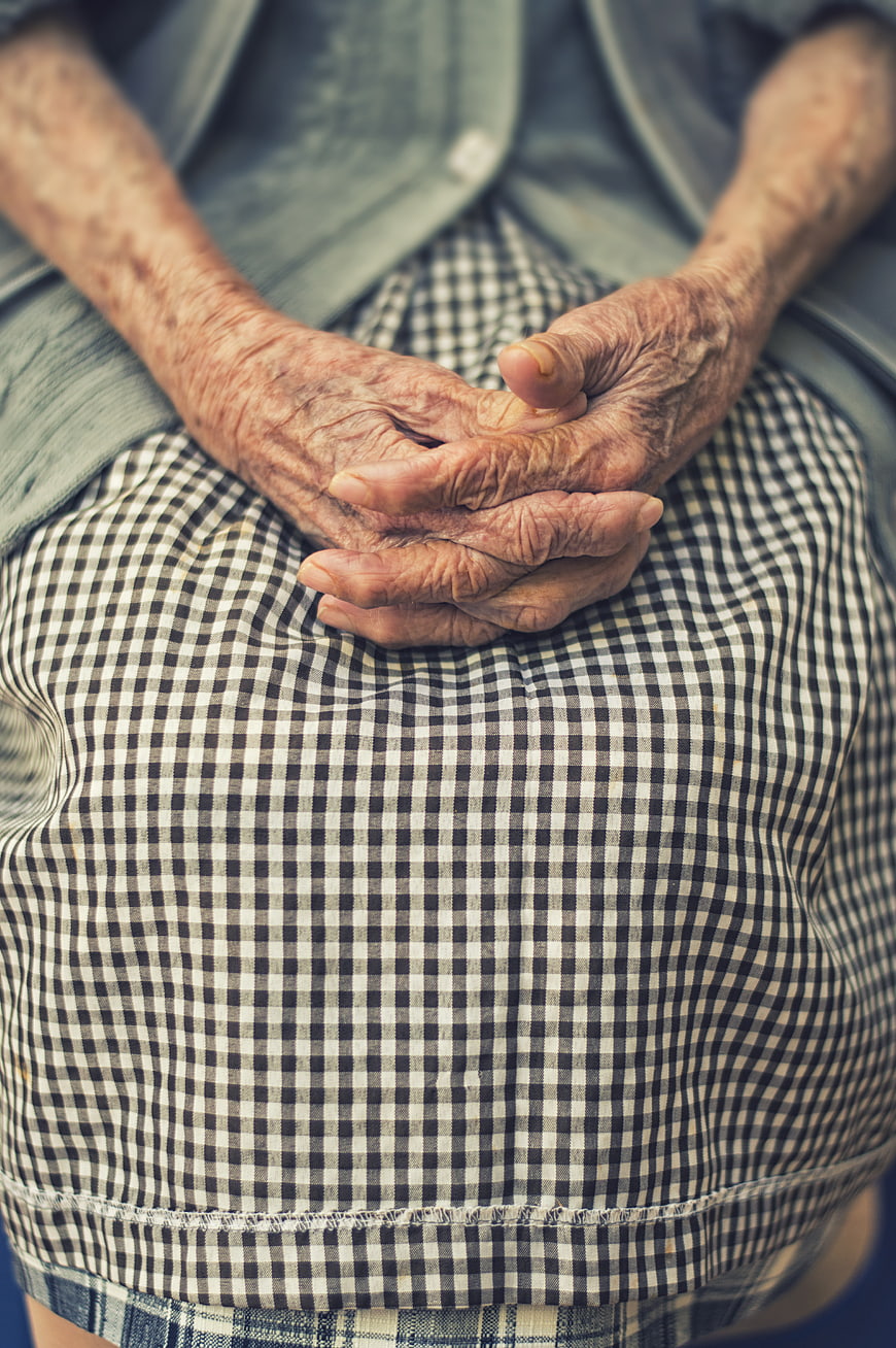 Close-up of elderly woman's wrinkled hands resting on checkered dress