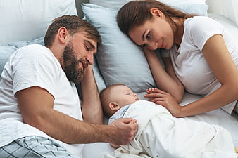 Happy Parents Watching Sleeping Newborn Baby in Bed