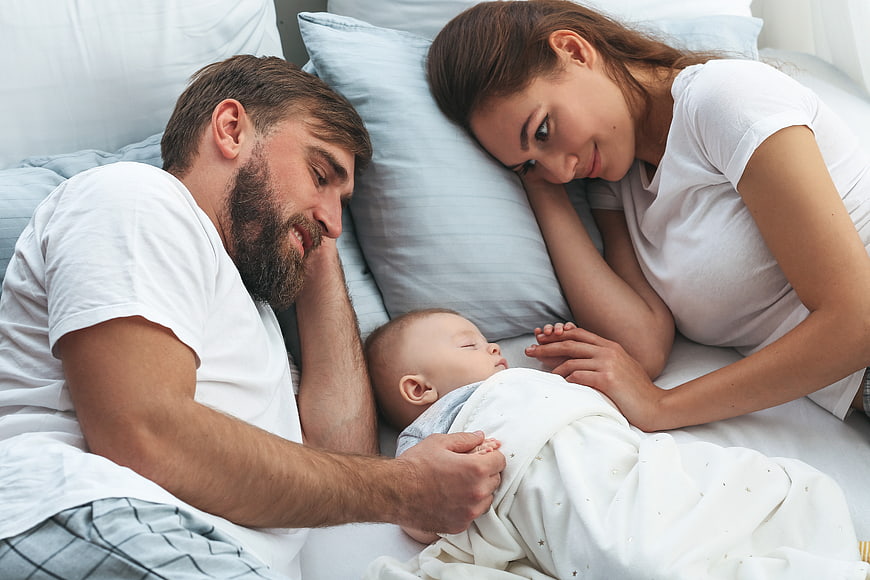 Happy Parents Watching Sleeping Newborn Baby in Bed