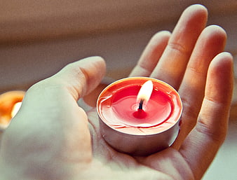 Hands holding a lit red tea light candle
