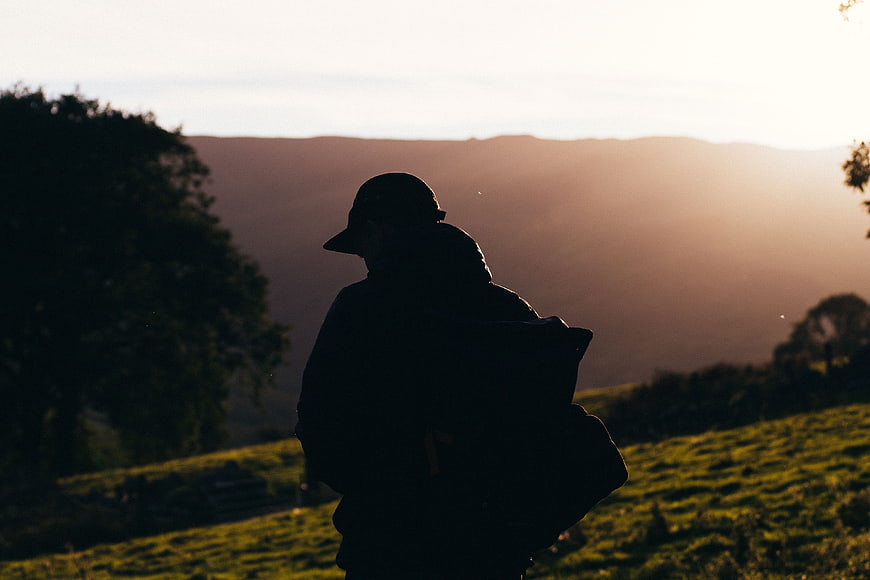 Silhouette of Hiker with Backpack on Grassy Hill at Sunset