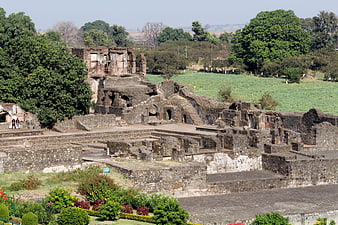 Ancient stone ruins of Hampi with lush green fields and trees