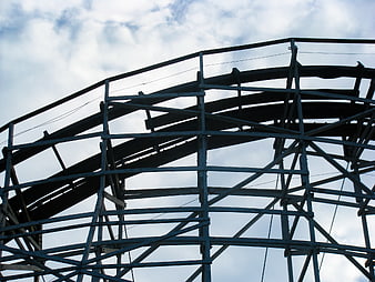 Low angle view of wooden roller coaster tracks against cloudy sky