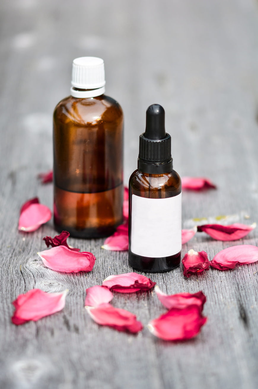 Amber essential oil bottles with rose petals on gray wood