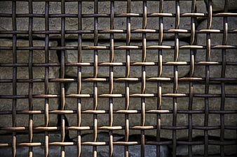Close-up of rusted metal wire mesh fence against stone wall