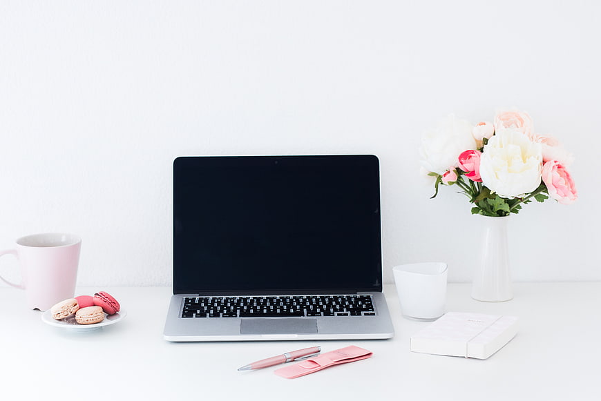 Minimalist workspace with laptop, pink macarons, and flowers