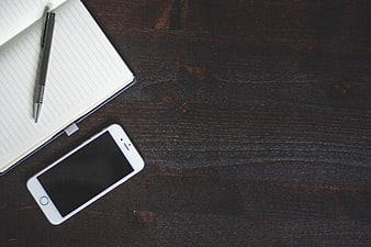 White Smartphone, Pen, and Notebook on Dark Wood Desk