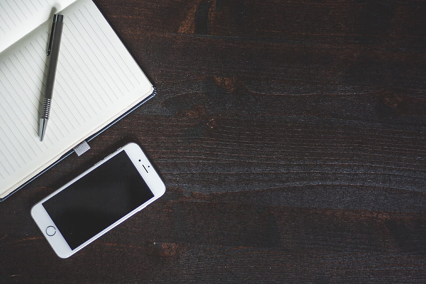 White Smartphone, Pen, and Notebook on Dark Wood Desk