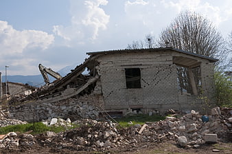 Demolished concrete house with rubble and excavator