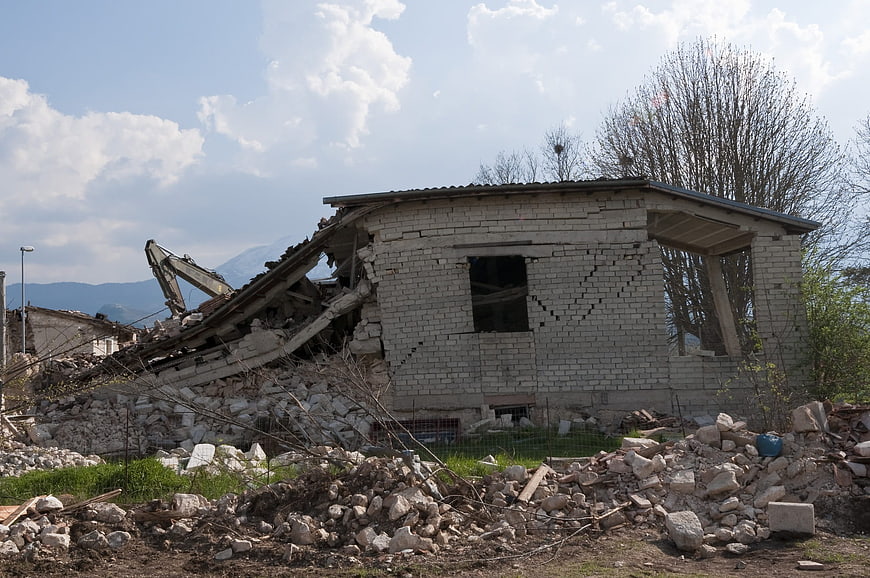 Demolished concrete house with rubble and excavator