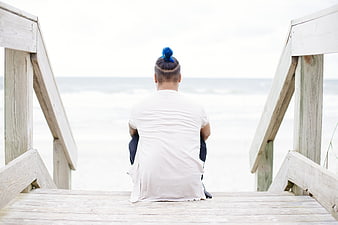 Man with blue hair bun sitting on wooden beach stairs