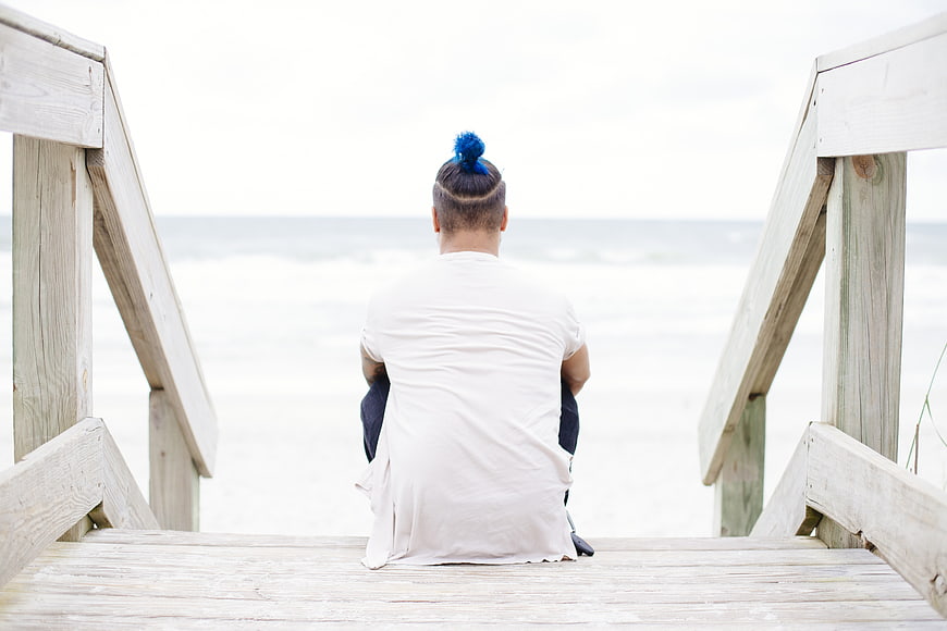 Man with blue hair bun sitting on wooden beach stairs