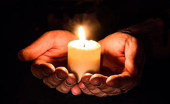 Hands holding a lit candle in the dark