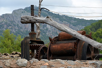 Rusty vintage mining machinery with wooden beam against mountain backdrop