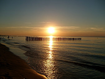 Sunset over calm sea with wooden groynes and golden reflection