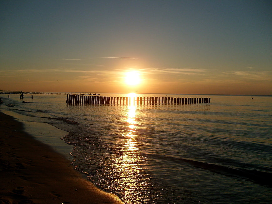 Sunset over calm sea with wooden groynes and golden reflection