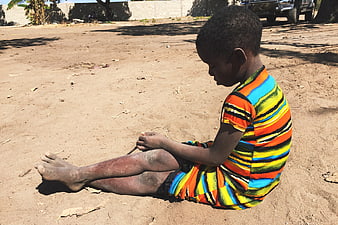 Young African boy sitting on dusty ground in colorful striped shirt