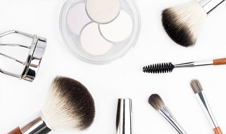 Flat lay of makeup brushes, palette, and eyelash curler on white
