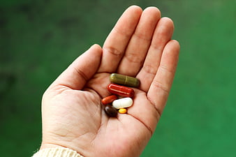 Open Hand Holding Assorted Medication Capsules Against Green Background