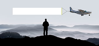 Silhouette of man on mountain peak with airplane towing banner