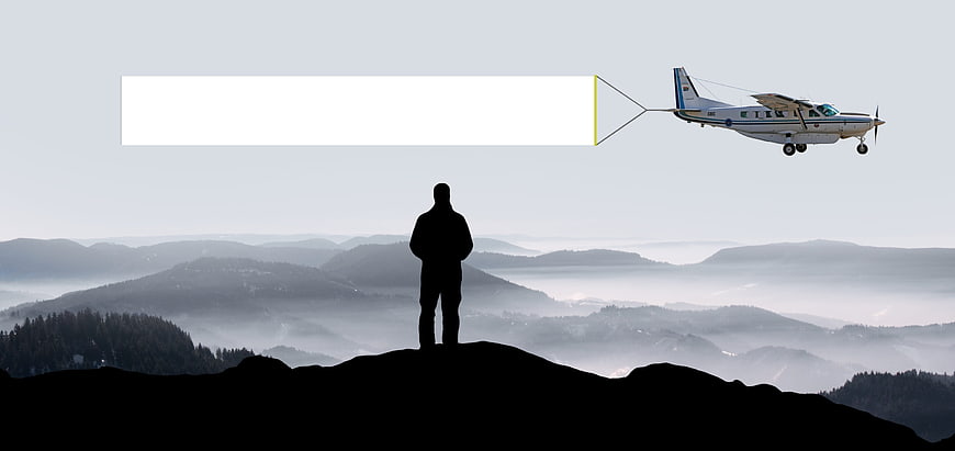Silhouette of man on mountain peak with airplane towing banner
