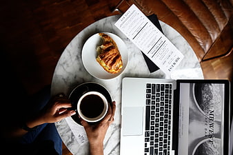 Flat lay of coffee, croissant, and laptop on marble table