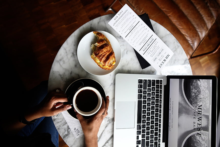 Flat lay of coffee, croissant, and laptop on marble table