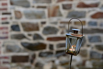 Rusty metal lantern with lit candle against blurred stone wall background