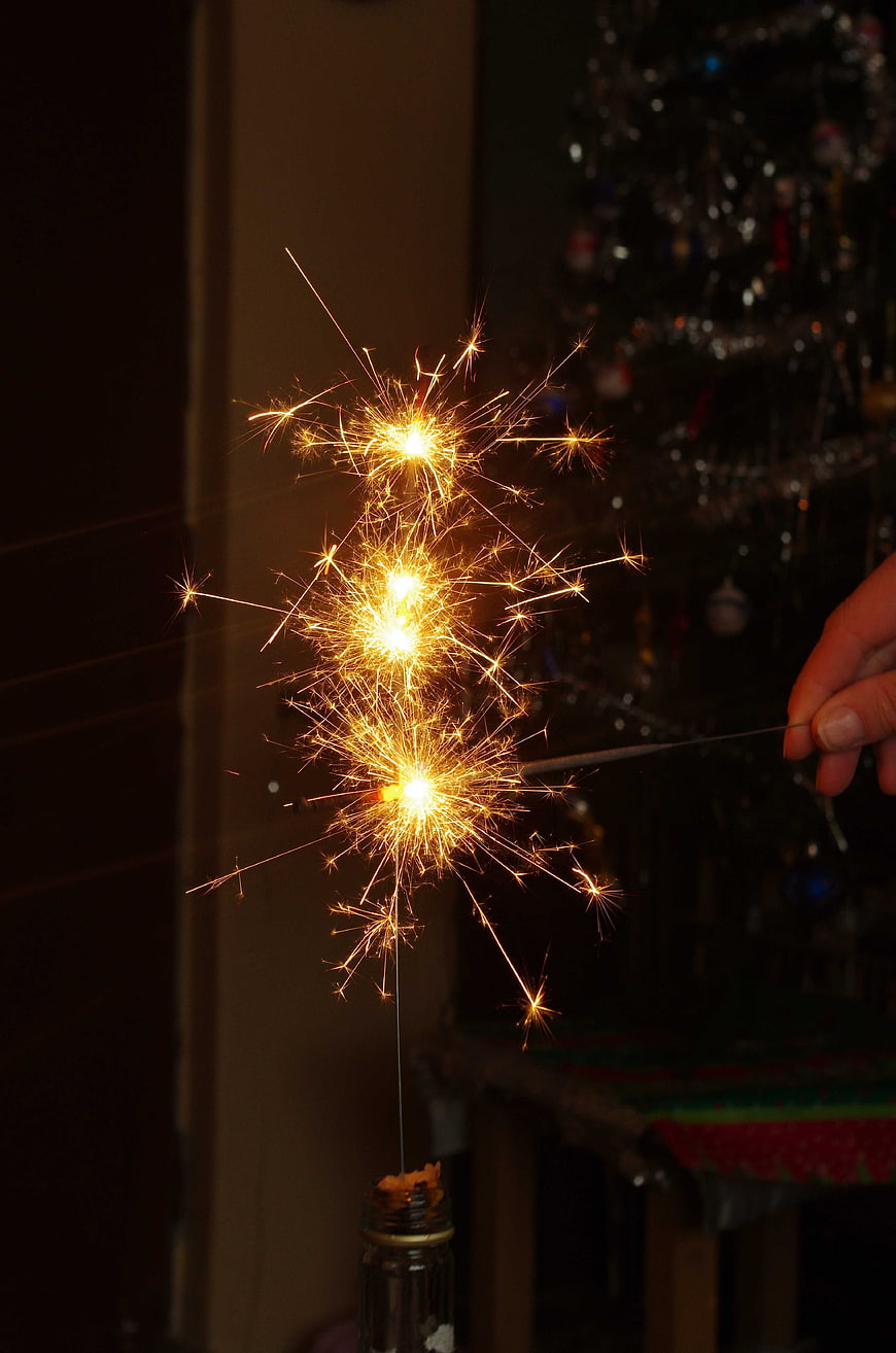 Hand Lighting Sparkler Near Christmas Tree